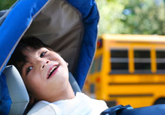 Smiling young boy in adaptive chair with school bus in the background