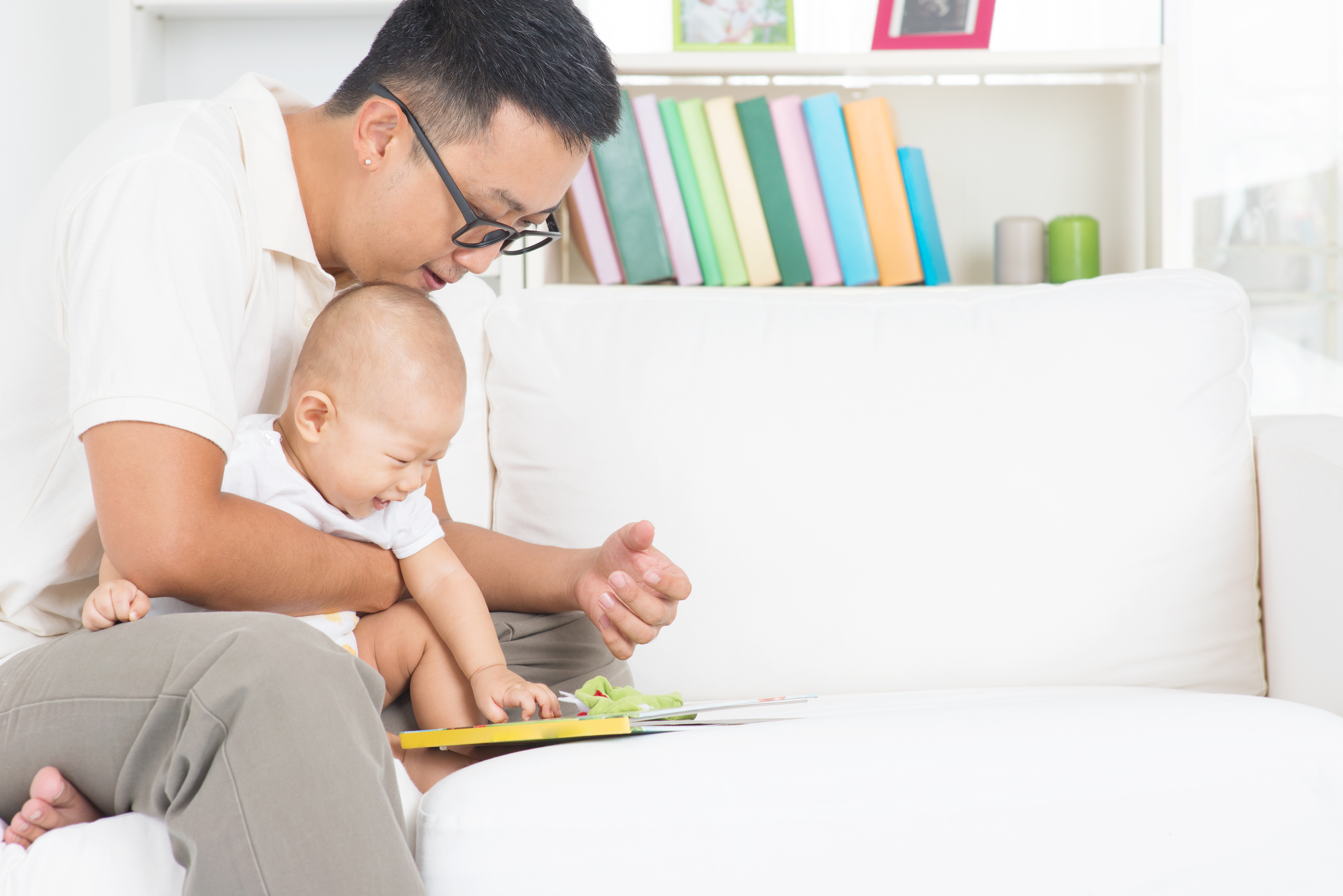 Father and child reading story book on sofa.