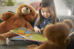 Young girl reading a picture book to her teddy bears