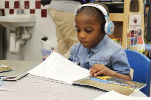 Young child reading story book while simultaneously listening to it on headphones