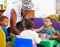 Teacher helps children working on an art project around the table