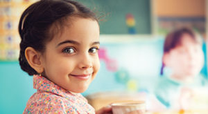 Young girl in a classroom setting smiles at camera